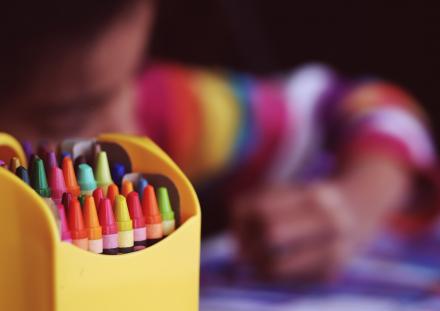 Box of brightly coloured crayons with child in the background