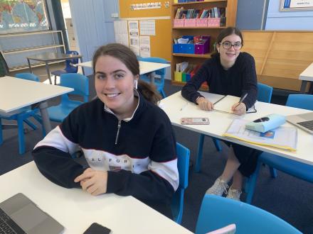 a picture of two girls sitting at desks at school.