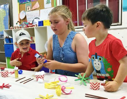 Older female student working with early years students in classroom