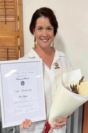 Kim wearing white shirt with certificate and flowers